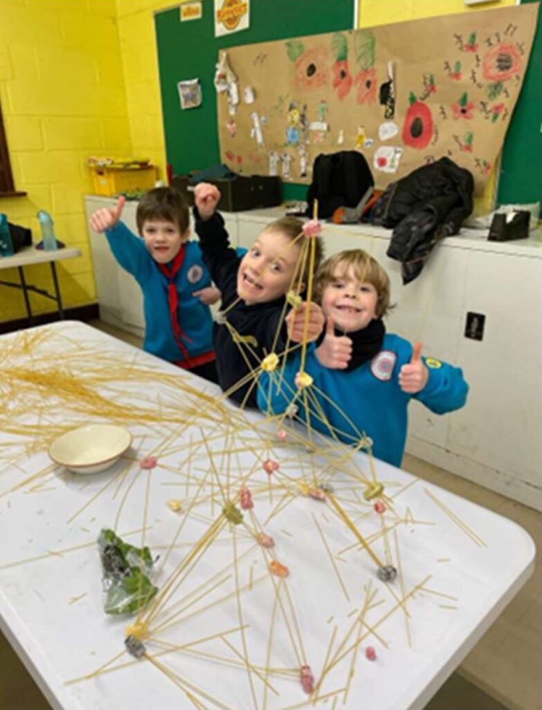 Three Beaver Scouts making structures from spaghetti, and giving thumbs up